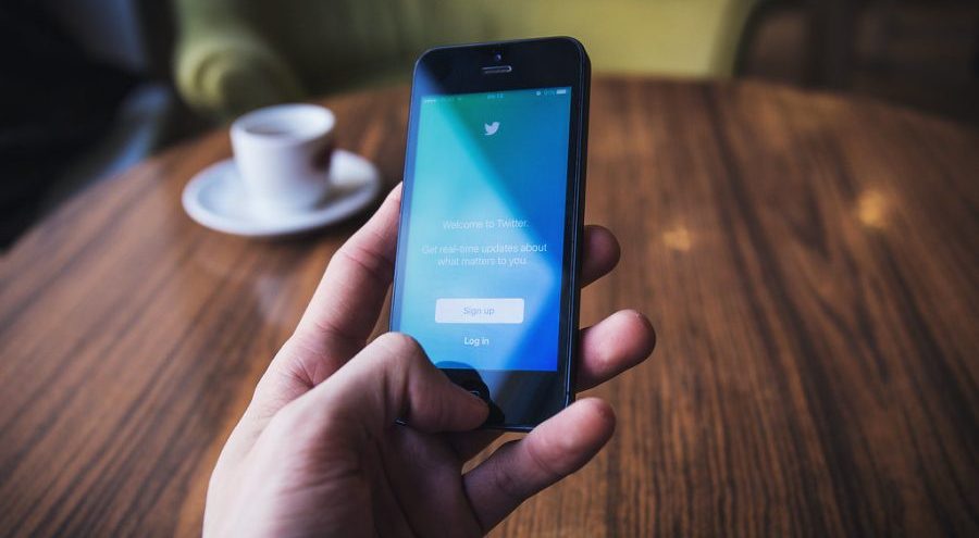 A hand holding a phone displaying the login screen for Twitter.